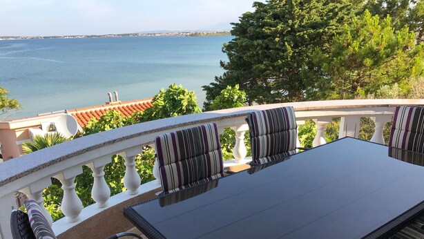 A balcony with a table and chairs, overlooking a body of water and a distant coastline. - Nice apartment in Privlaka (Privlaka)