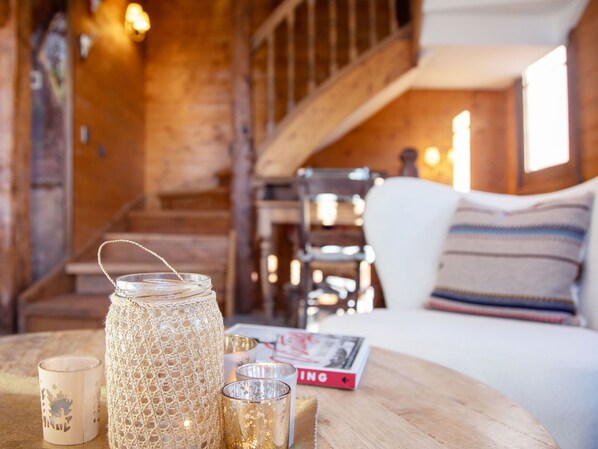 A cozy room with a wooden staircase, a white chair, and a table with candles and a book.