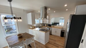 A modern kitchen with white cabinets, a central island, a gas stove, a microwave, and a stainless steel range hood. - Cute centrally located home! (Cedar Falls)