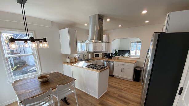 Una cocina moderna con alacenas blancas, una isla central, una estufa a gas, un microondas y una campana extractora de acero inoxidable.