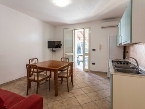 A compact kitchen with a dining area, a TV mounted on the wall, and a sliding glass door leading to an outdoor area.