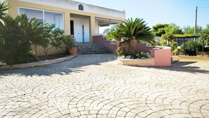 Un bâtiment sur lequel on peut lire l’inscription « Villa Cosimo », avec une cour dallée, un chemin en pierre, des palmiers et une pergola équipée de sièges.