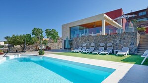 A modern pool area with clear blue water, a stone wall, and lounge chairs.