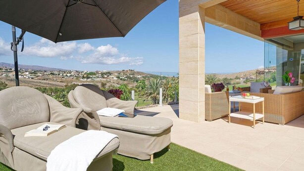A modern outdoor lounge area with a sofa and a table, a large umbrella, and a view of the landscape.