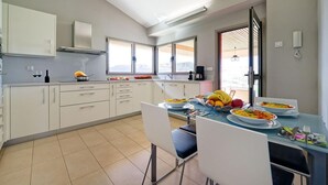 A modern kitchen with white cabinets, a dining table set for four, and a large window providing natural light.