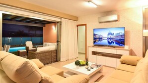 A modern hotel room with a balcony, a flat-screen TV, a white coffee table, and a sofa.