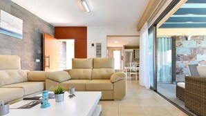 A modern living room with a sectional sofa, a white coffee table, and a wicker chair. There is a glass door leading to a balcony.