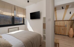 Relax in this serene bedroom with a large bed, flat-screen TV, and a balcony offering a view of the outdoors.