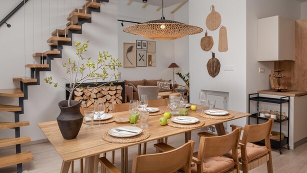 A modern dining area with a wooden table set for four, surrounded by chairs. A staircase with wooden steps and black railings is visible to the left. - Amazing home in Rizvanusa (Gospic)