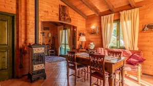 L’intérieur d’un chalet confortable en bois, avec un coin repas, des murs en bois, une cheminée et une grande fenêtre agrémentée de rideaux.