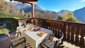 Un espace extérieur abrité, aménagé pour les repas, avec une table pour deux personnes, offrant une vue sur un paysage montagneux.