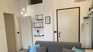 Un salon moderne avec un canapé gris, des coussins bleus et gris, un radiateur blanc et une porte à cadre noir.