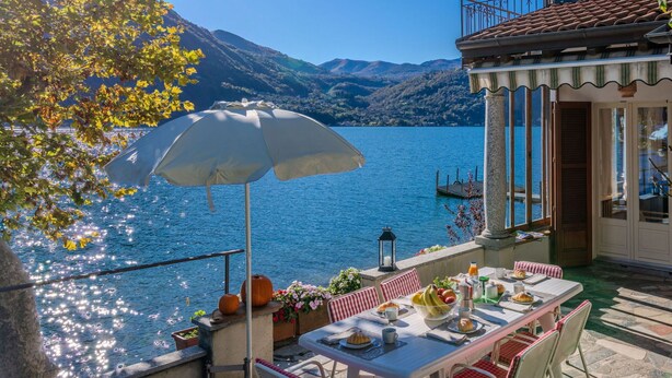 Une terrasse avec une table dressée pour le petit-déjeuner, donnant sur un lac et entourée de montagnes.