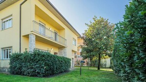 A yellow building with a balcony, stone pillars, and a well-maintained garden with hedges and a tree. - Beautiful apartment for 6 guests with WIFI, TV and patio (Pietrasanta)