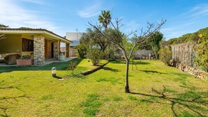 A house with a stone pillar, a covered patio, and a well-maintained lawn. - Beautiful private villa for 4 people with WIFI, A/C, TV, terrace and panoramic view (Villasimius)