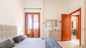 A bedroom with a bed, a nightstand, a dresser, a mirror, and a door leading to a dining area. - Beautiful private villa for 4 people with WIFI, A/C, TV, terrace and panoramic view (Villasimius)