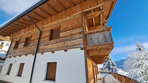 A wooden chalet with a white facade, multiple windows, and a wooden balcony.