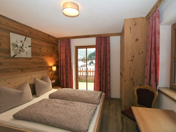 A cozy room with wooden walls, a bed with checkered bedding, a chair, and a window with curtains. - Nice apartment for 10 people with WIFI, TV and patio (Wildschönau)