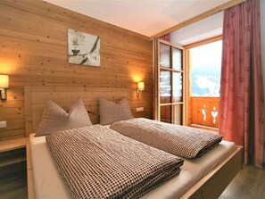 Une pièce aux murs lambrés, comprenant un lit, deux oreillers, une table de chevet, une lampe fixée au mur et une fenêtre donnant sur les montagnes.
