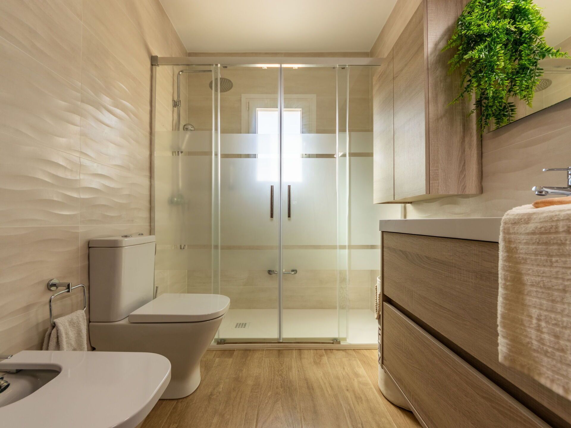 Un baño moderno con cabina de ducha de vidrio, inodoro, lavamanos y tocador con espejo.