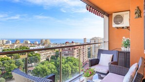 A balcony with wicker furniture, a view of the city, and an air conditioning unit.