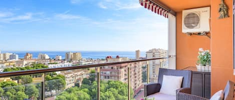 A balcony with wicker furniture, a view of the city, and an air conditioning unit.