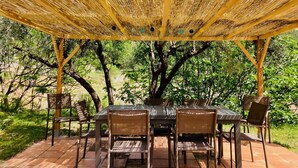 Un espace de restauration en plein air, agrémenté d’une pergola, et entouré d’arbres et de verdure.