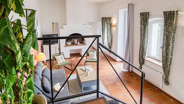 Un vaste espace de vie comprenant un canapé, une table basse et un téléviseur. Un escalier mène à un autre niveau, et une grande plante est visible.