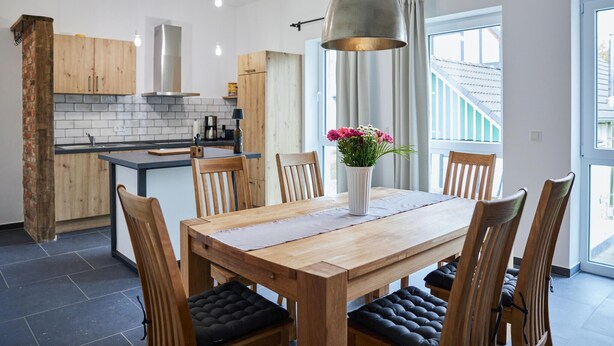 A modern kitchen with wooden cabinets, a central island, and a dining area with a wooden table and chairs.