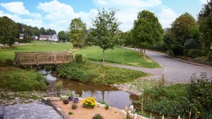 A serene park with a wooden bridge, a small pond, and a paved walkway.