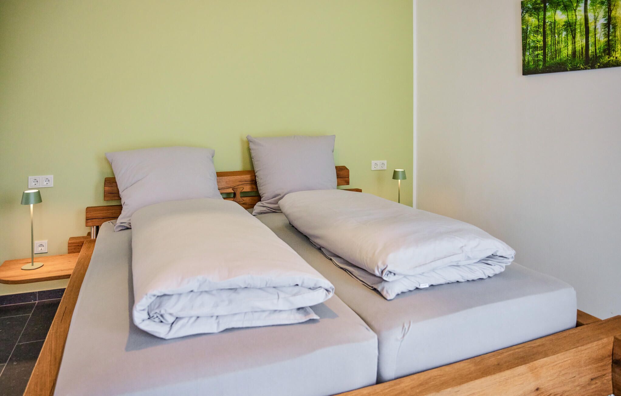 Una cama doble con sábanas de tonos claros, un cabecero de madera y una pared verde.