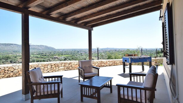 Eine überdachte Terrasse mit Holzmöbeln, einem Tischkicker und einer Steinwand.