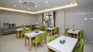 A modern dining area with green chairs and white tables, a kitchen in the background, and a large window with curtains. - Greentree Inn Hefei Government Cultural District South District Provincial Hospital Nanqu Hotel (Hefei)