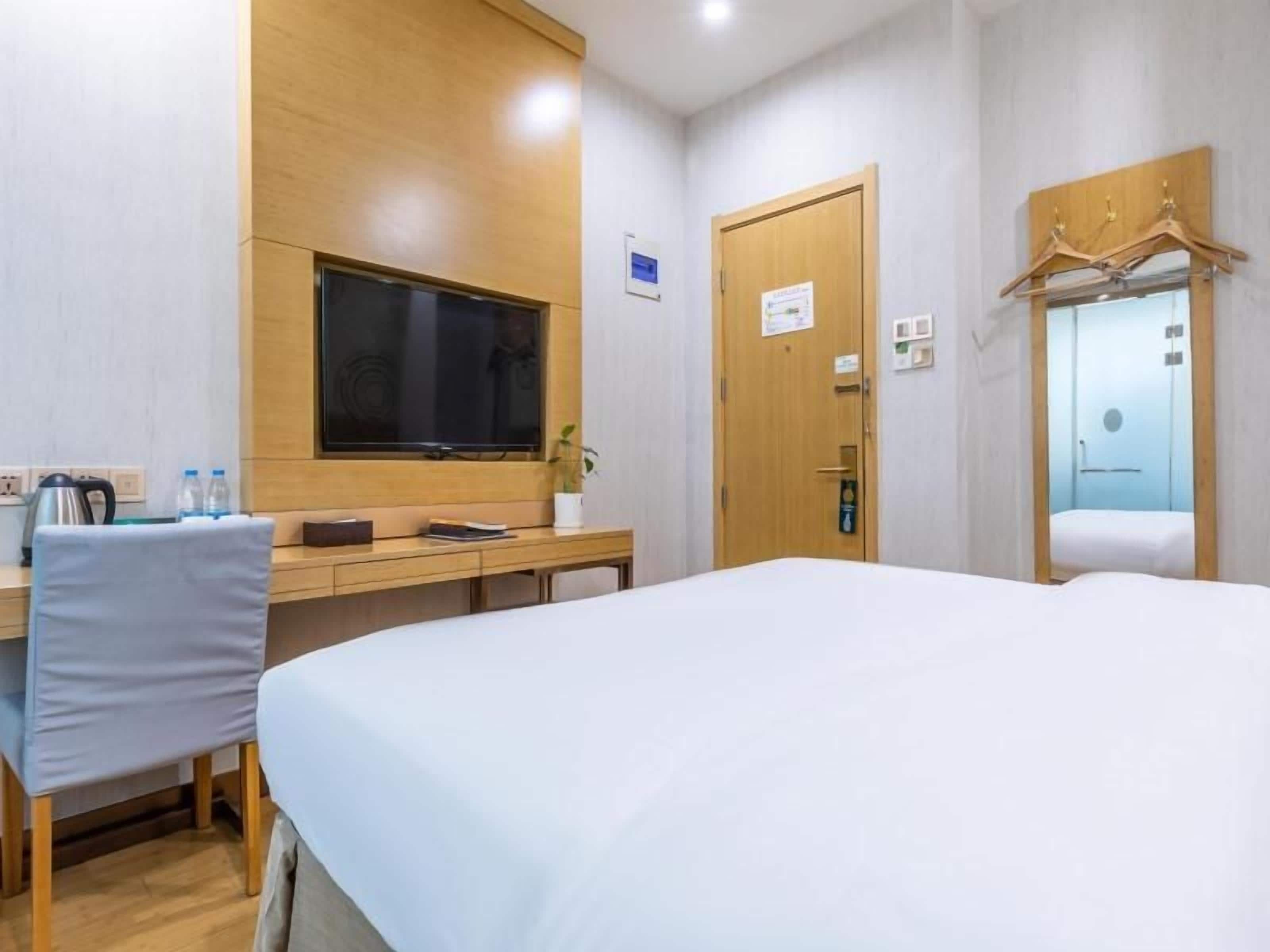 A hotel room with a bed, a desk with a chair, a television, and a wardrobe with a mirror.