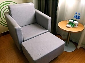 A grey armchair with a matching ottoman in a hotel room. A small round table with a white mug and green packets is beside the chair. - Greentree Inn Hefei Government Cultural District South District Provincial Hospital Nanqu Hotel (Hefei)
