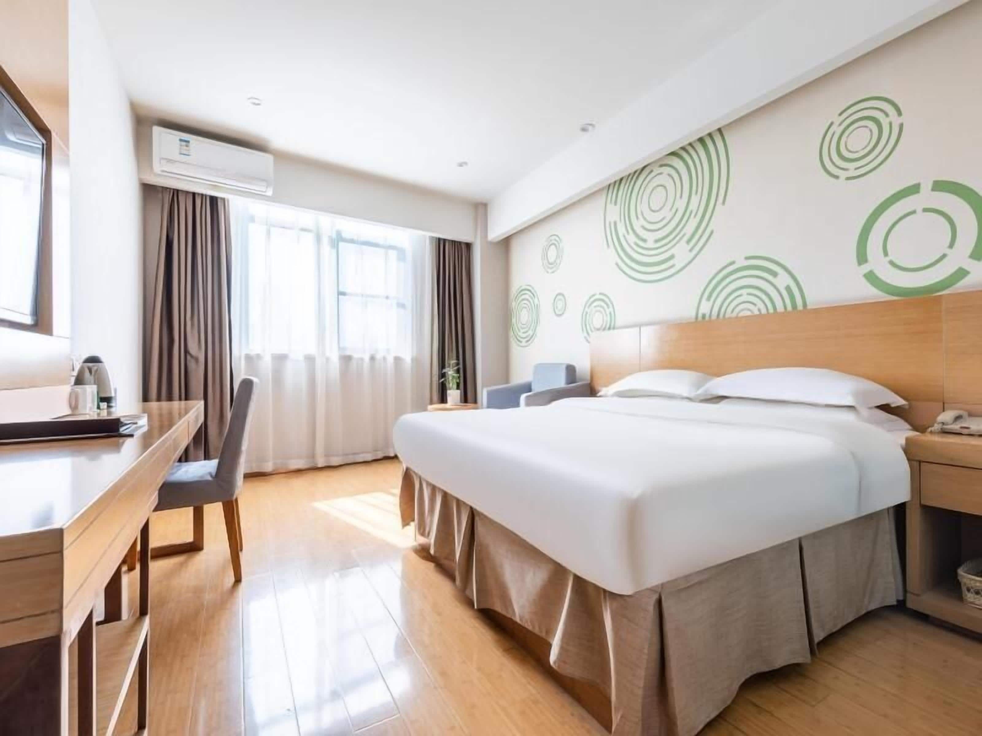 Quarto de hotel com cama, escrivaninha, cadeira, ar condicionado e parede com desenhos circulares.