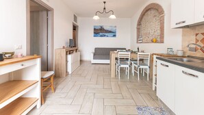 A compact kitchen with a dining area, wooden flooring, white cabinetry, and a hanging light fixture. - Nice apartment for 5 people with A/C, WIFI and TV (Follonica)