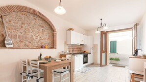 A cozy kitchen with a stone wall backsplash, wooden dining table, and white cabinets. - Nice apartment for 5 people with A/C, WIFI and TV (Follonica)