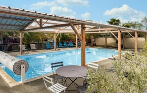 A pool area with a covered patio, lounge chairs, and a table.