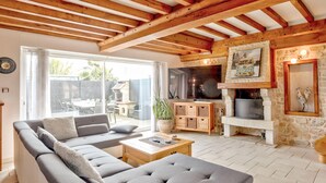 A spacious living area with a grey sofa, wooden beams, a stone fireplace, and a TV. - Beautiful home in l'étang-bertrand (L'Étang-Bertrand)