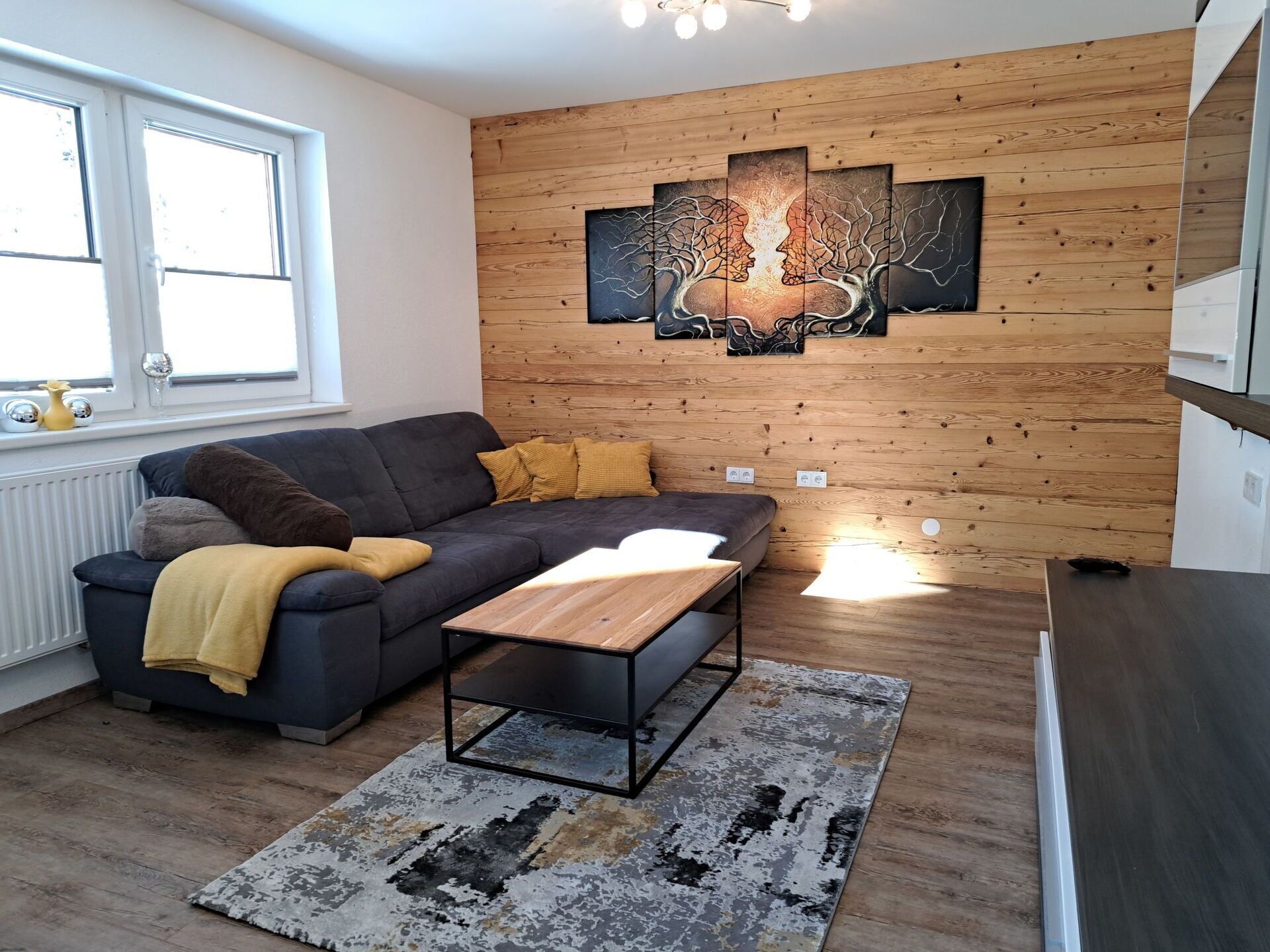 A modern living room with a grey sofa, wooden coffee table, and a large abstract painting on the wall.
