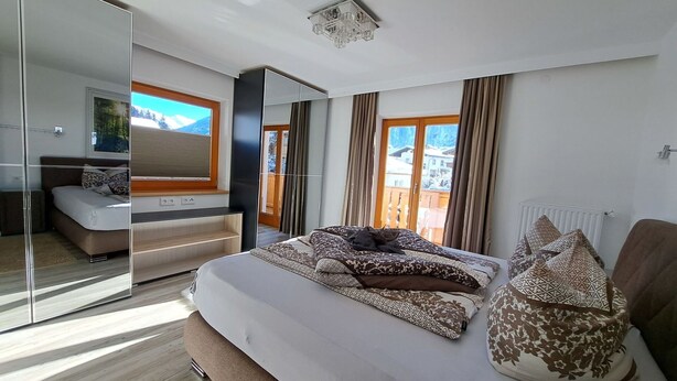 A modern bedroom with a large bed, a glass wardrobe, a view of the outdoors, and a ceiling light fixture. - Cosy apartment for 8 people with WIFI, TV and balcony (Grossdornau)