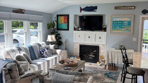 Een woonkamer met een open haard, een televisie en een eetgedeelte met een tafel en stoelen.