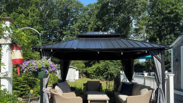Een overdekt terras met wicker meubilair, een pergola en uitzicht op een achtertuin.