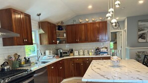 Een moderne keuken met houten kastjes, een marmeren aanrechtblad en roestvrijstalen apparatuur.