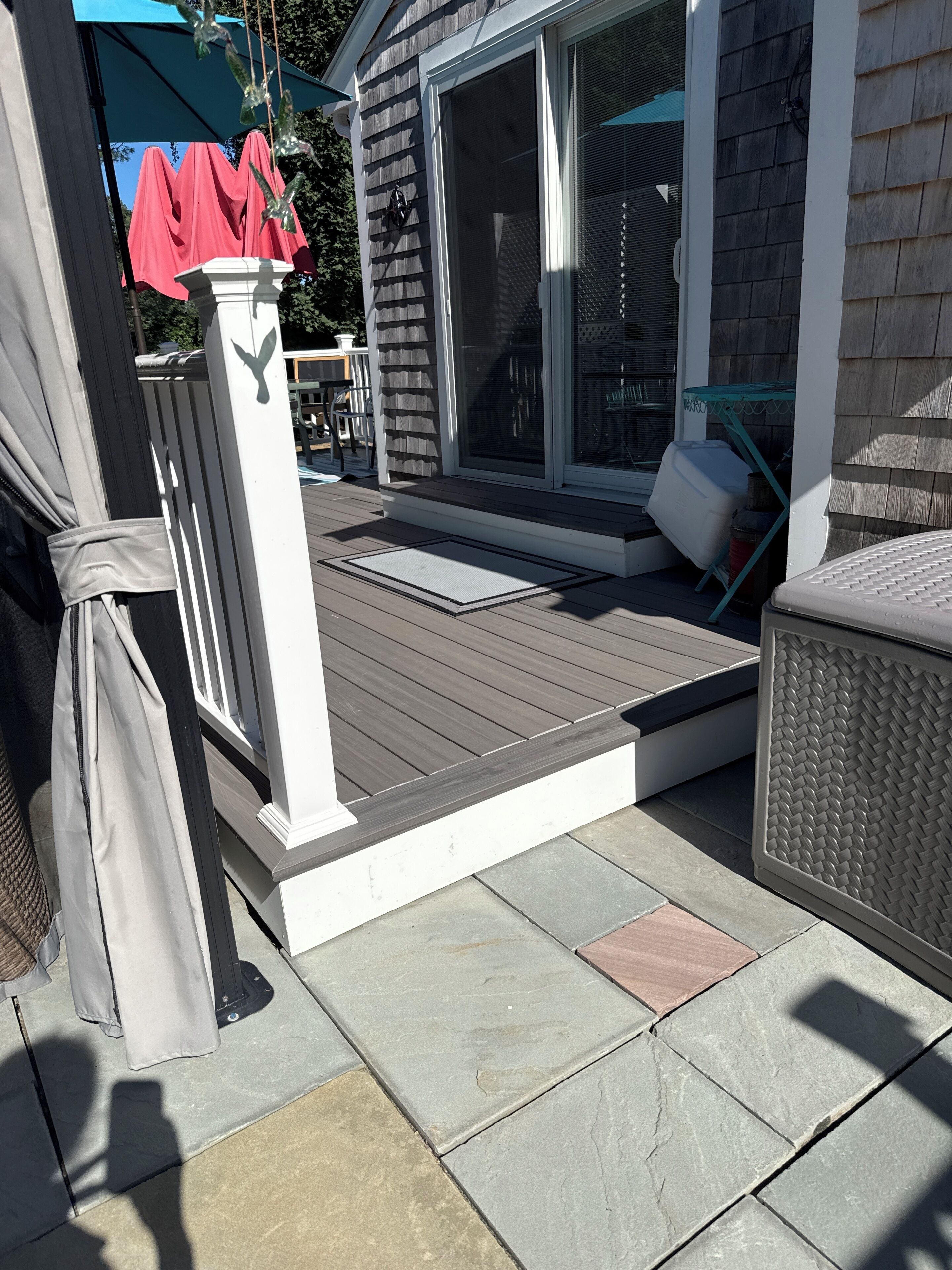 A deck with a white railing, a covered patio area, and a sliding glass door leading to a covered outdoor seating area.