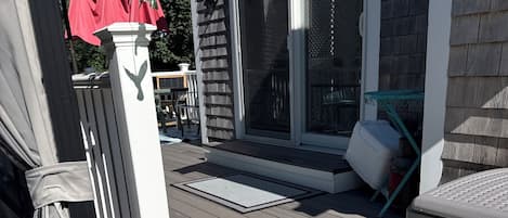 A deck with a white railing, a covered patio area, and a sliding glass door leading to a covered outdoor seating area.