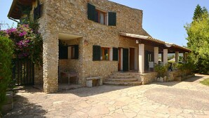 A stone house with a covered porch, steps leading to the entrance, and a garden with pink flowers. - Wonderful private villa for 6 guests with WIFI, private pool, TV, patio and panoramic view (Inca)