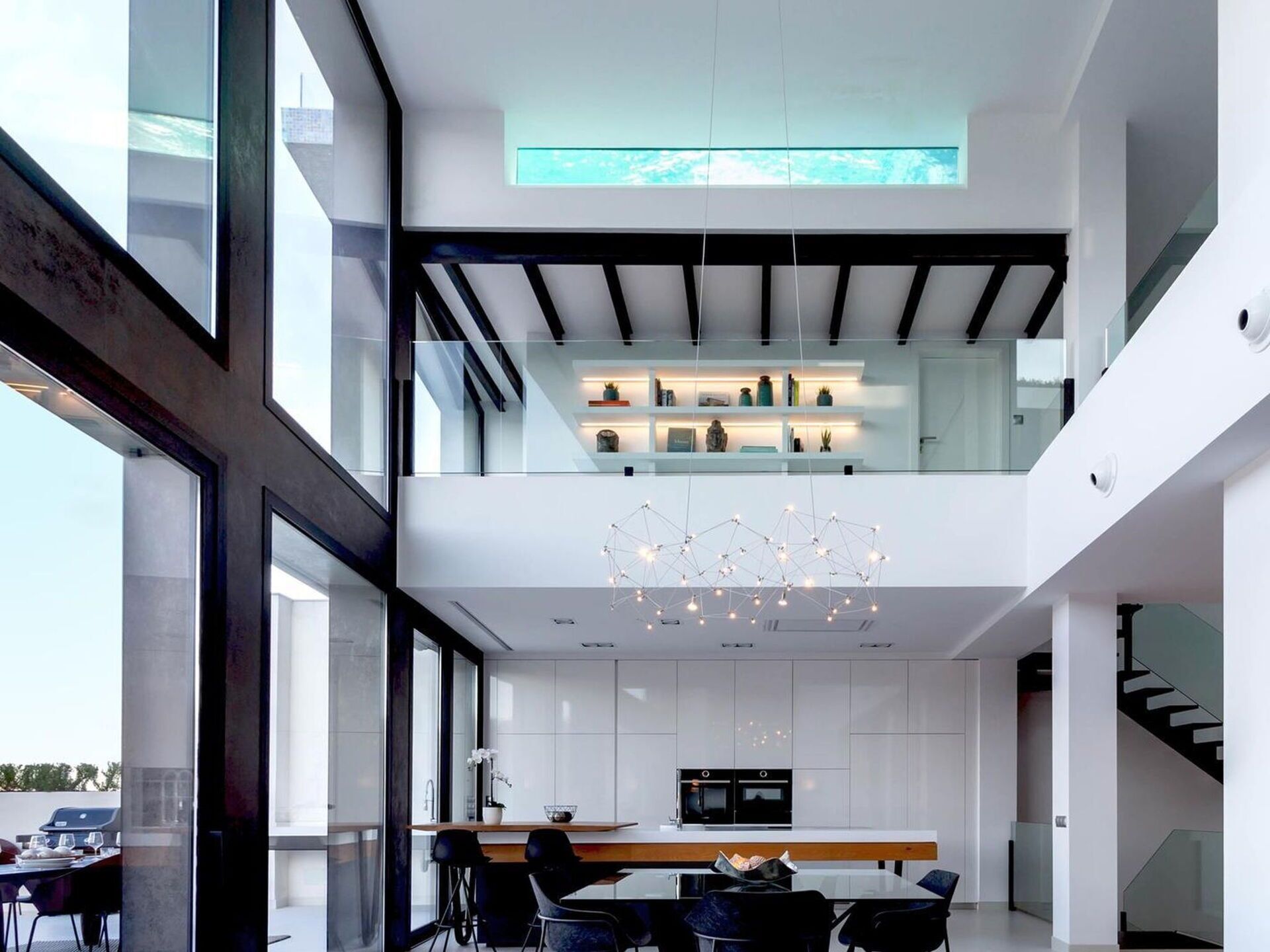 A modern, multi-level kitchen with a central island, glass railings, and a hanging light fixture.
