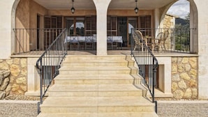 A stone building with a central staircase leading to a covered patio area with outdoor seating.